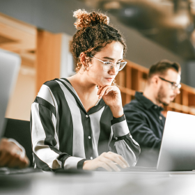 Focused young professional working on a laptop in a modern open-plan office, illustrating how Adaptive Experiences support deep concentration and productivity in digital workplaces.
