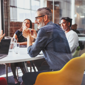 Diverse team collaborating around a meeting table in a modern office, highlighting how Adaptive Experiences foster engaging, personalized interactions in workplace environments.