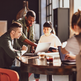 Creative startup team collaborating around a laptop in a bright modern office, demonstrating how Adaptive Experiences enable flexible, user‑centric teamwork in digital workspaces.